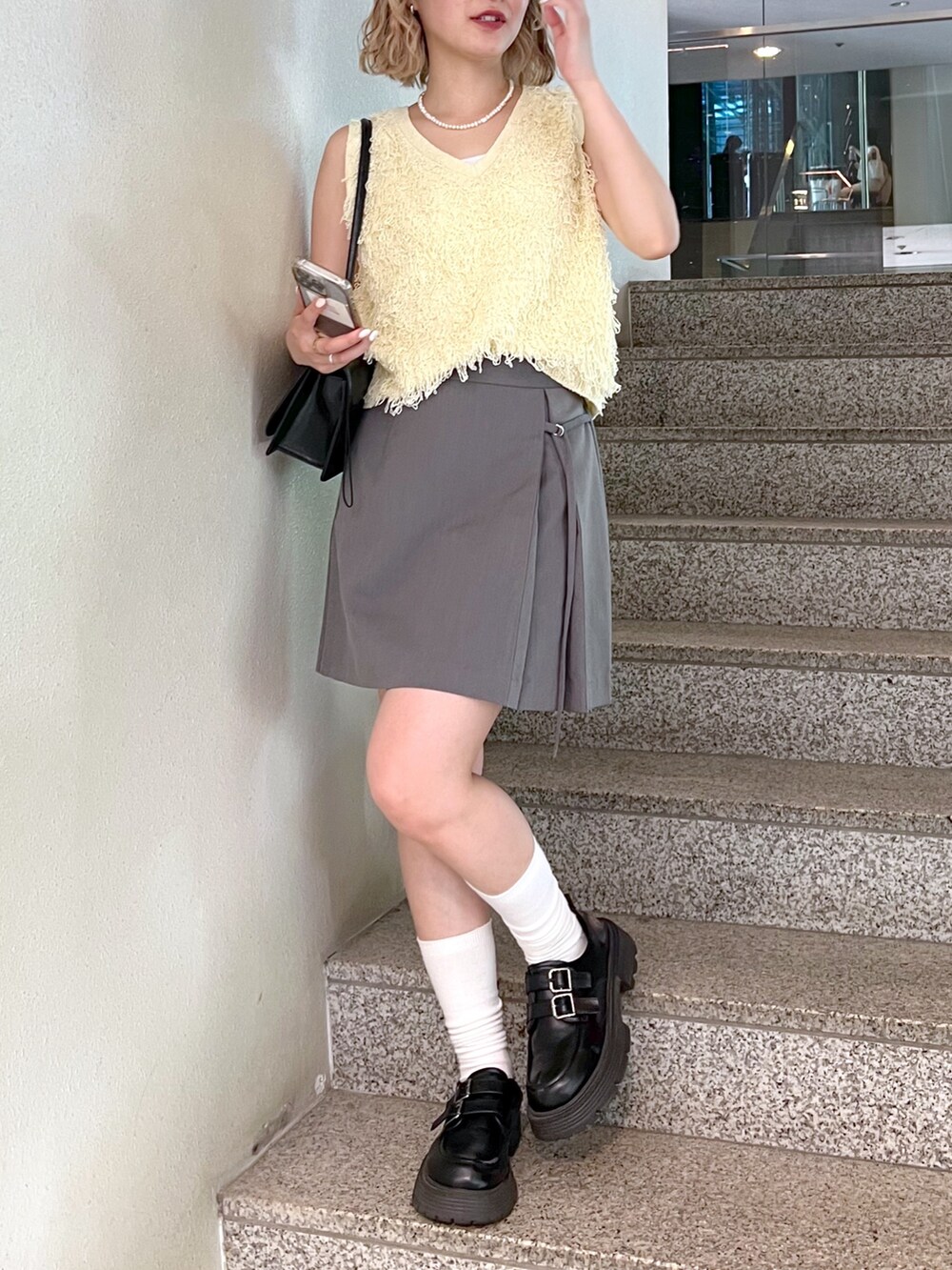 グレー系のスカート、イエロー系のニット/セーター、ホワイト系のキャミソールを着用したレディースの夏コーディネートの5枚目の写真