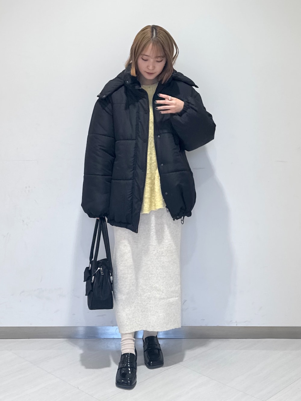 ブラック系のダウンジャケット/コート、イエロー系のニット/セーター、ブラック系のトートバッグを着用したレディースの冬コーディネートの2枚目の写真