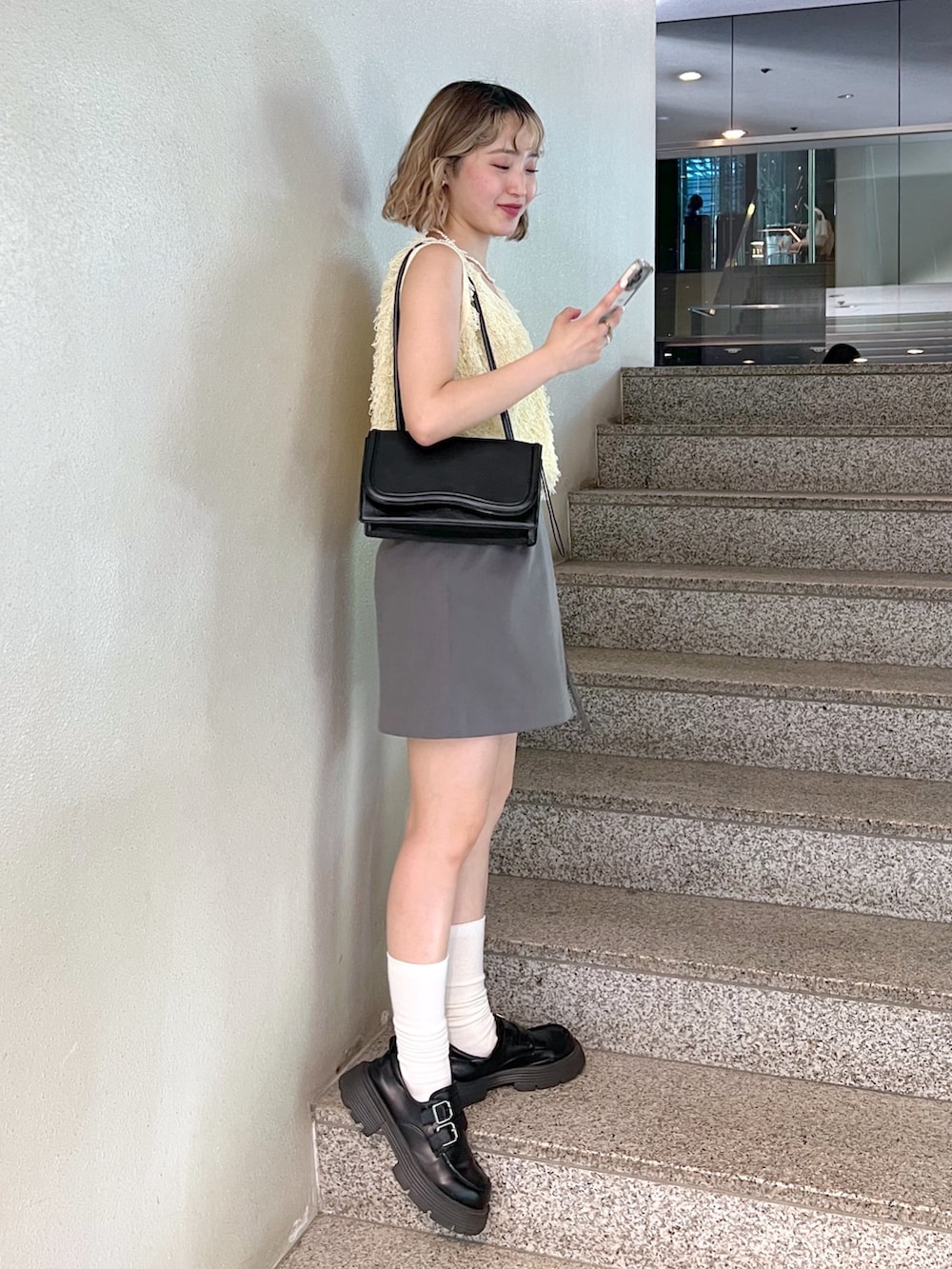 グレー系のスカート、イエロー系のニット/セーター、ホワイト系のキャミソールを着用したレディースの夏コーディネートの2枚目の写真