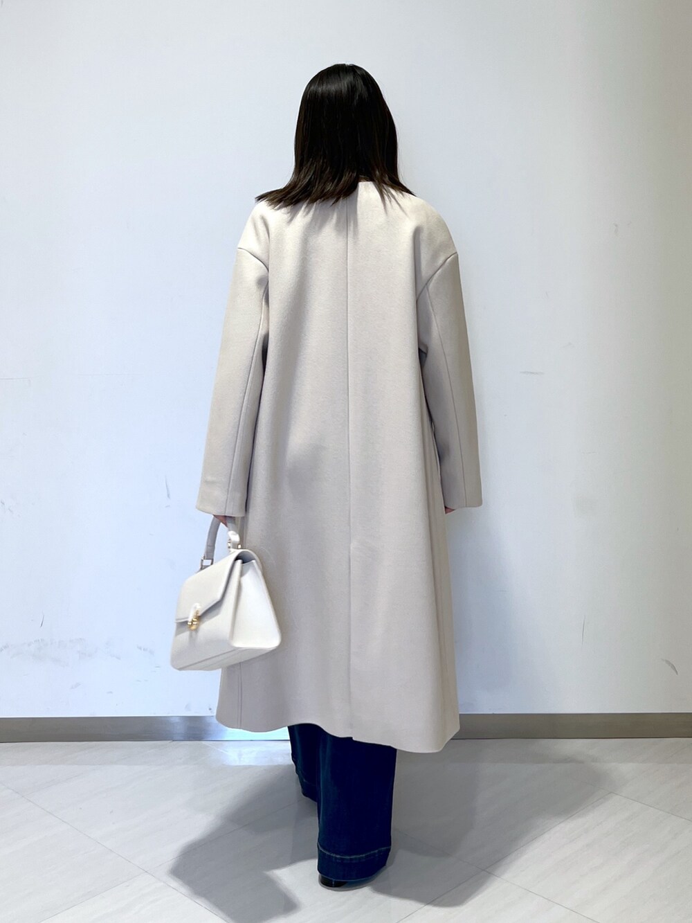 ベージュ系のノーカラーコート、ブラック系のシャツ/ブラウス、ブルー系のデニムパンツを着用したレディースの冬コーディネートの4枚目の写真