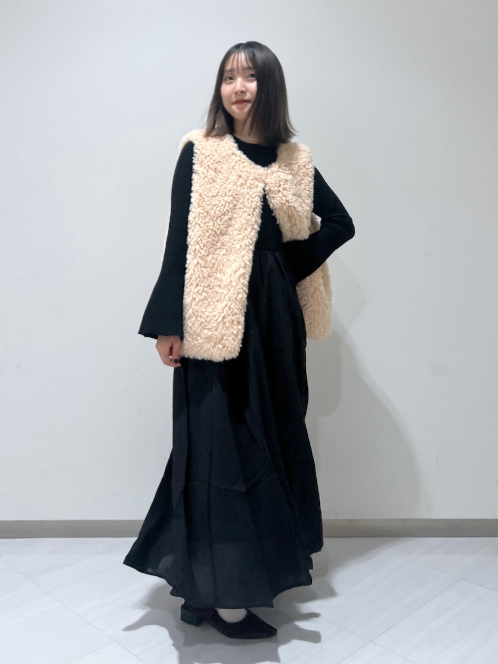 ブラック系のワンピース、ベージュ系のベスト、ブラウン系のバレエシューズを着用したレディースの秋コーディネートの5枚目の写真