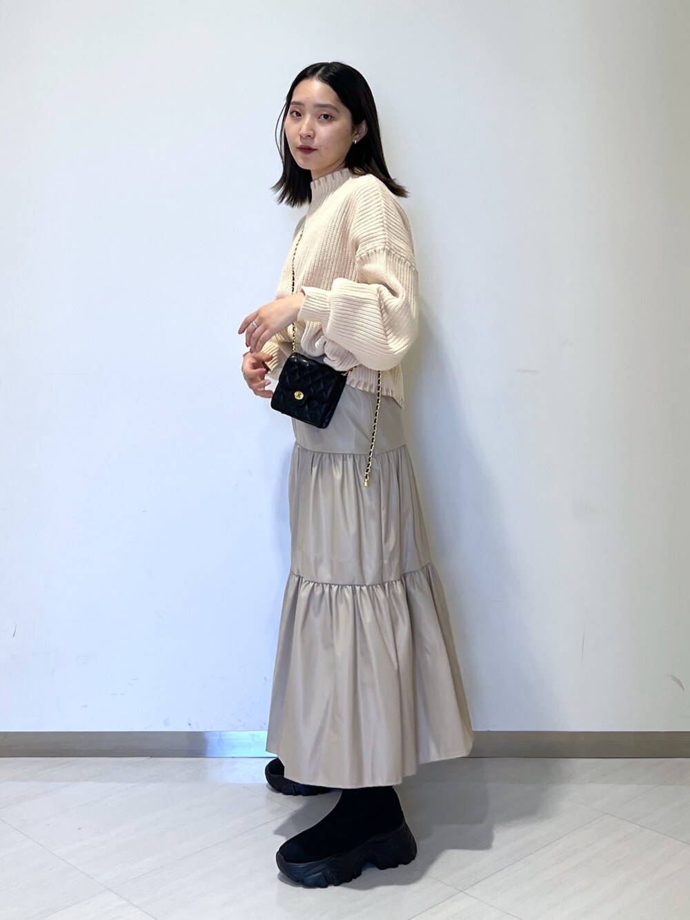 ベージュ系のスカート、ホワイト系のニット/セーター、ブラック系のショルダーバッグを着用したレディースの冬コーディネートの3枚目の写真