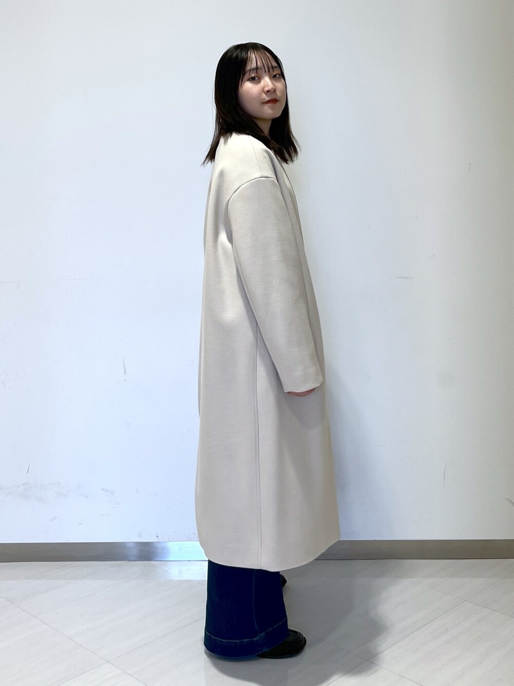 ベージュ系のノーカラーコート、ブラック系のシャツ/ブラウス、ブルー系のデニムパンツを着用したレディースの冬コーディネートの3枚目の写真