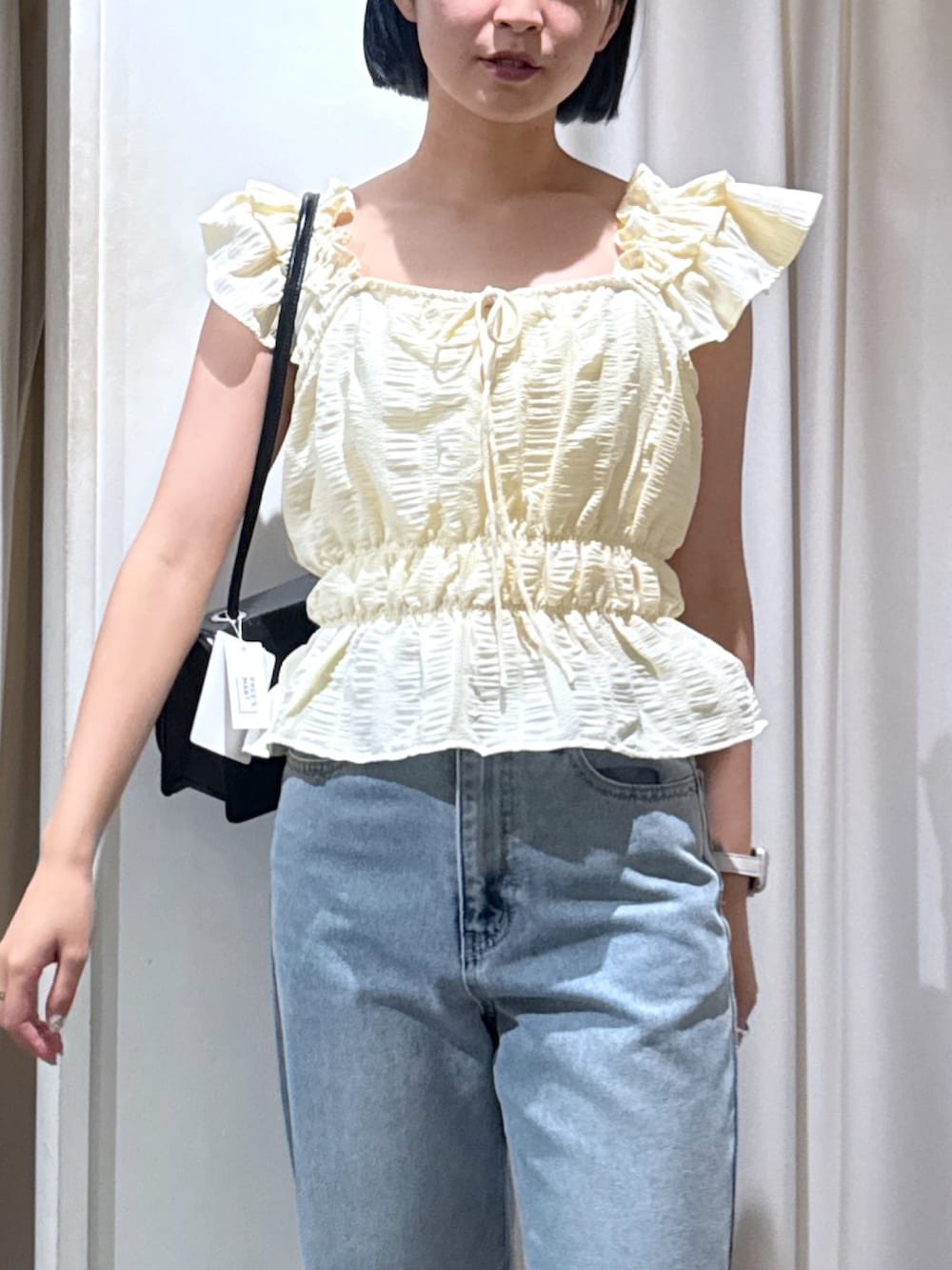 イエロー系のシャツ/ブラウス、ブラック系のショルダーバッグ、ブルー系のデニムパンツを着用したレディースの夏コーディネートの3枚目の写真