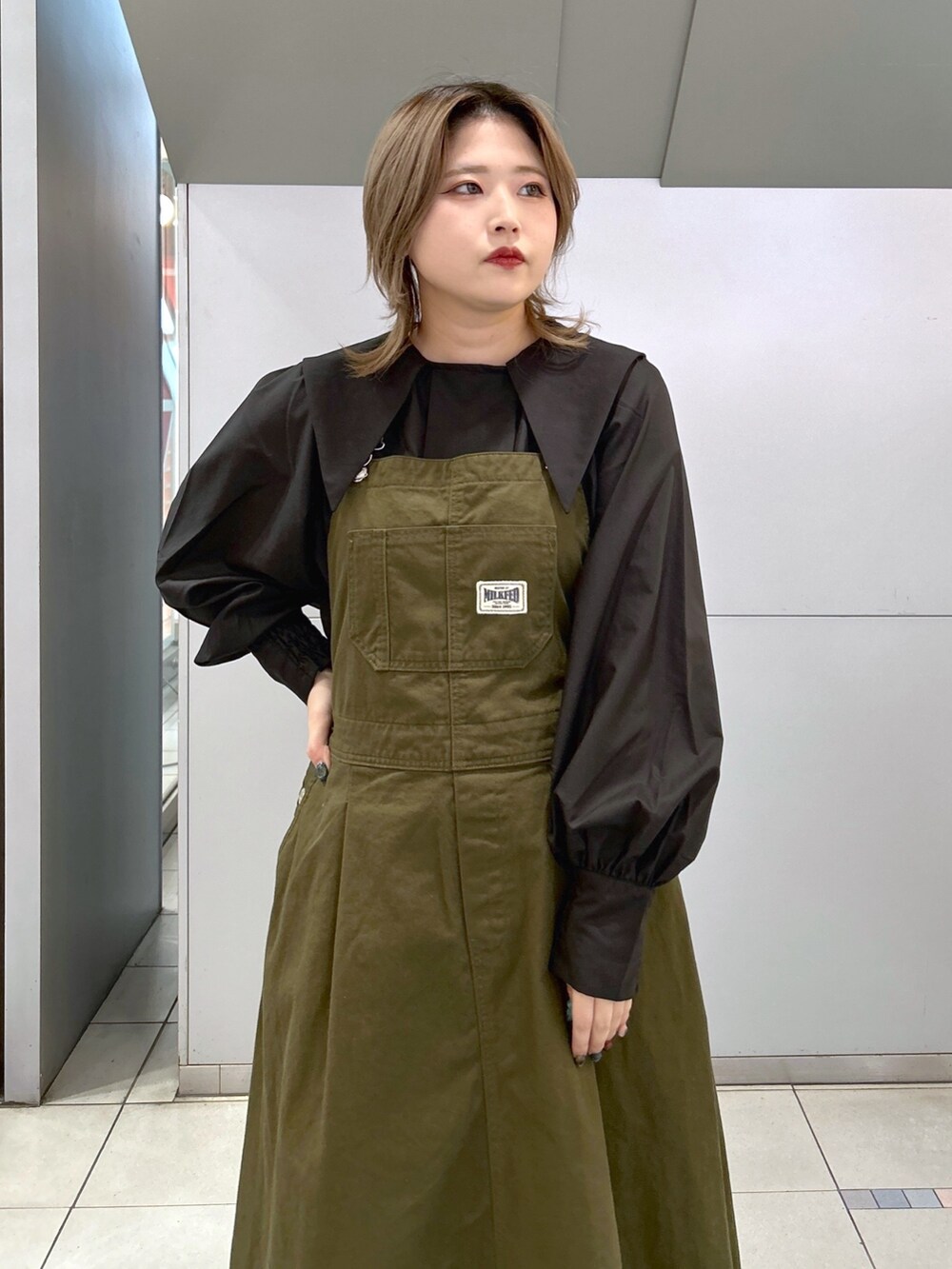 ブラック系のシャツ/ブラウス、グリーン系のジャンパースカート、ブラック系のブーツを着用したレディースの冬コーディネートの3枚目の写真