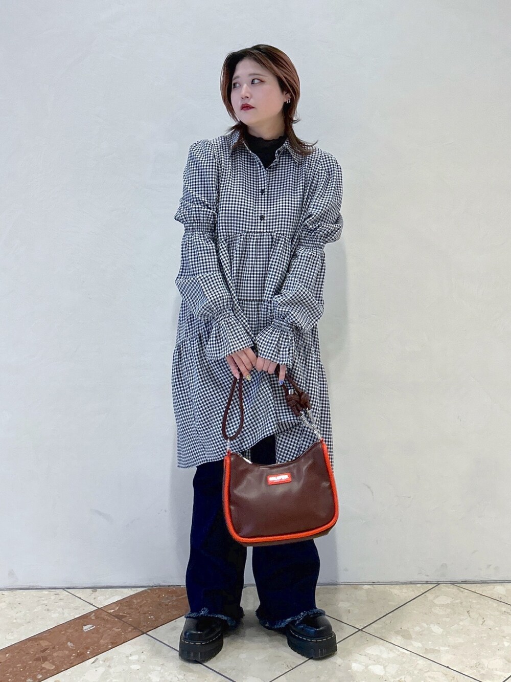 ブラック系のワンピース、ブルー系のデニムパンツ、ブラウン系のショルダーバッグを着用したレディースの春コーディネートの2枚目の写真