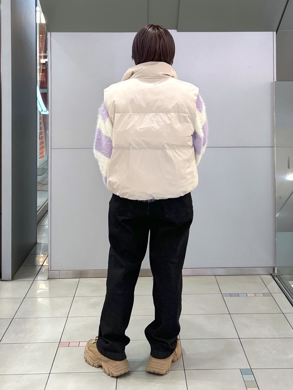 ブラック系のデニムパンツ、ベージュ系のスニーカー、ホワイト系のダウンベストを着用したレディースの秋コーディネートの3枚目の写真