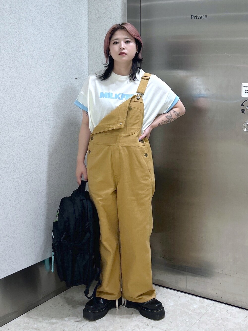 ベージュ系のサロペット/オーバーオール、ホワイト系のTシャツ/カットソー、ブラック系のブーツを着用したレディースの夏コーディネートの2枚目の写真