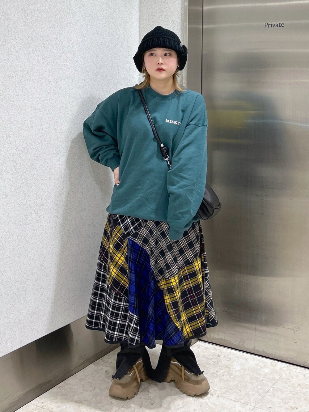 グリーン系のスウェット、ブラック系のショルダーバッグ、ブラック系のスカートを着用したレディースの冬コーディネートの2枚目の写真