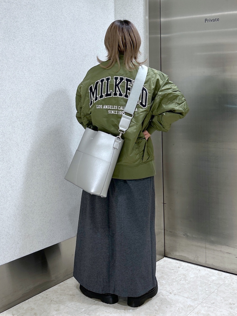 グレー系のワンピース、グリーン系のMA-1、シルバー系のショルダーバッグを着用したレディースの冬コーディネートの2枚目の写真