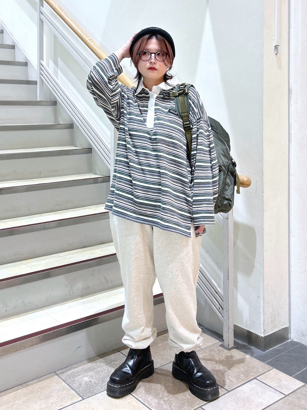 グリーン系のポロシャツ、ベージュ系のスウェットパンツ、グリーン系のバックパック/リュックを着用したレディースの冬コーディネートの2枚目の写真