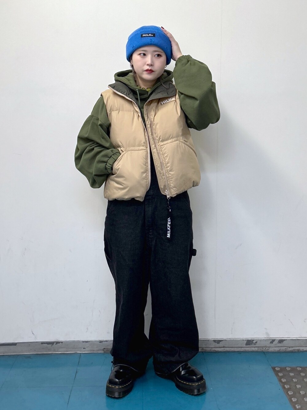 ベージュ系のダウンベスト、グリーン系のパーカー、ブラック系のサロペット/オーバーオールを着用したレディースの冬コーディネートの2枚目の写真