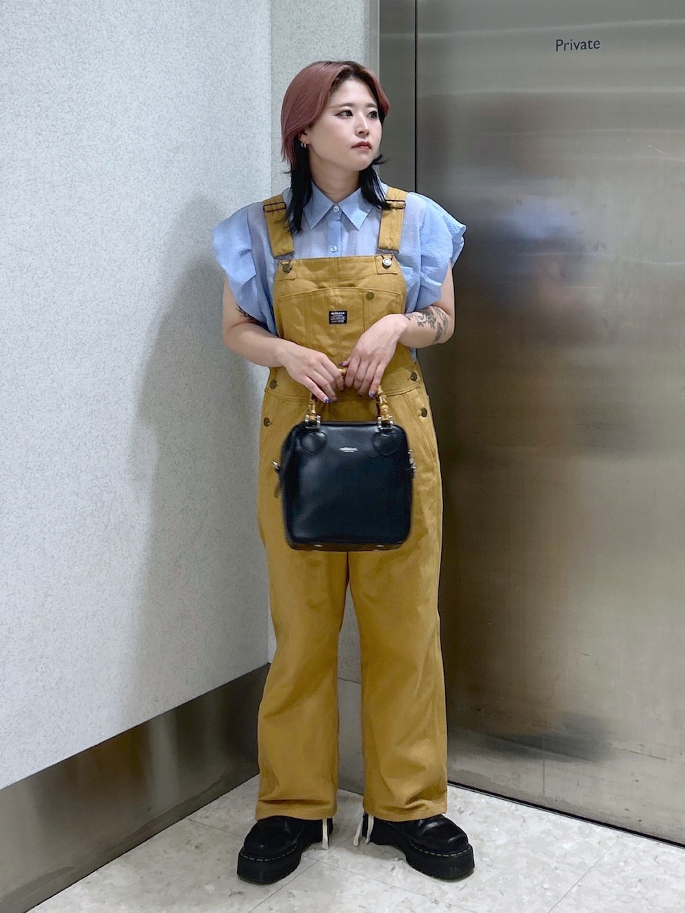 ブルー系のシャツ/ブラウス、ベージュ系のサロペット/オーバーオール、ブラック系のショルダーバッグを着用したレディースの夏コーディネートの2枚目の写真