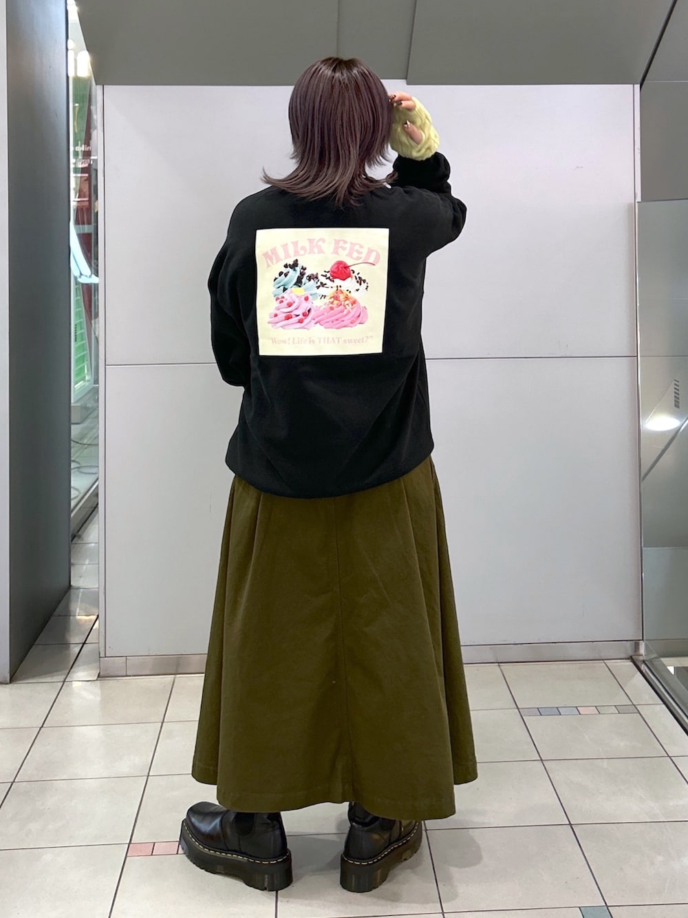 ブラック系のスウェット、グリーン系のジャンパースカート、シルバー系のショルダーバッグを着用したレディースの冬コーディネートの2枚目の写真