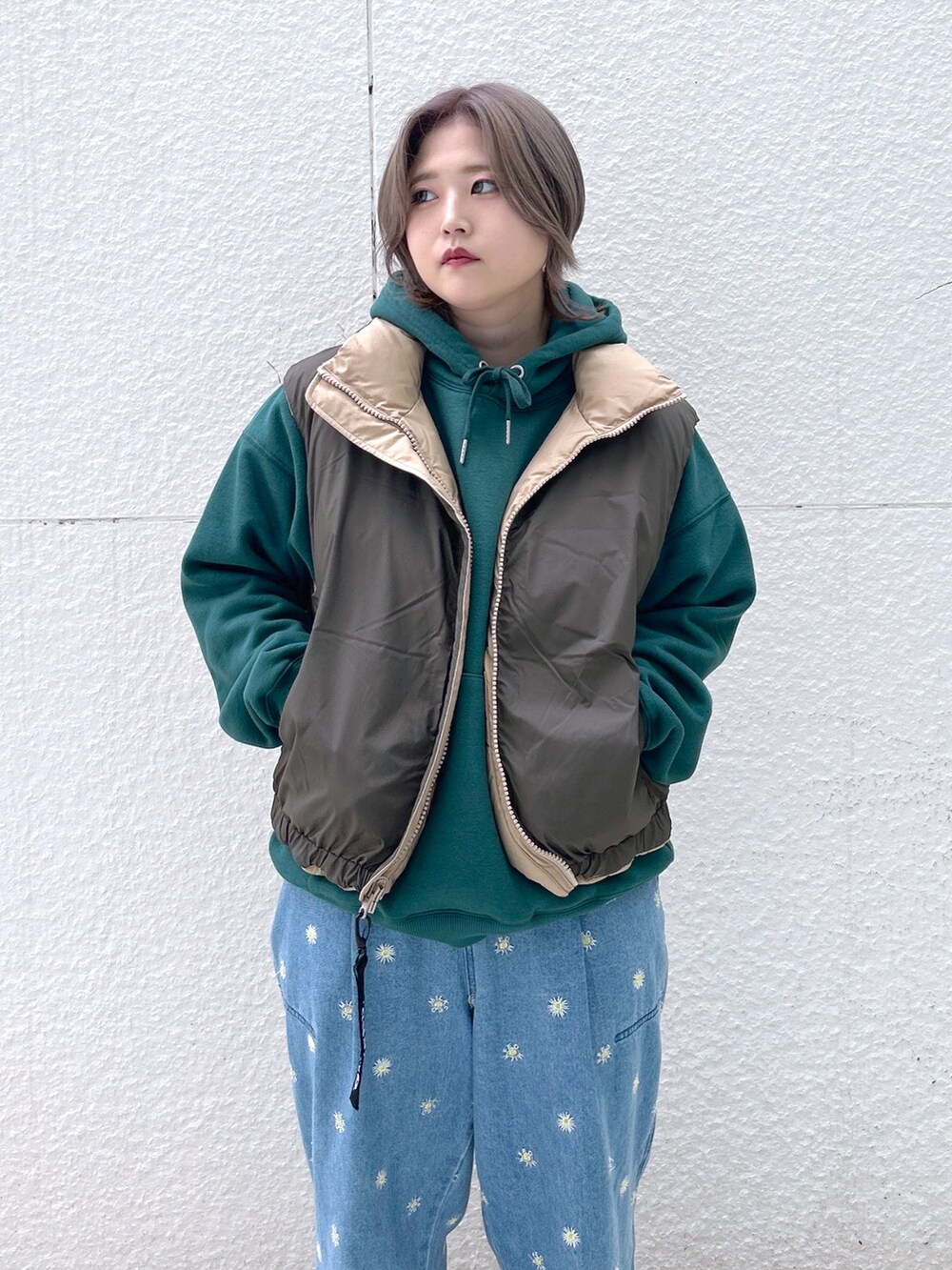 ベージュ系のダウンベスト、グリーン系のパーカー、ブルー系のデニムパンツを着用したレディースの秋コーディネートの3枚目の写真