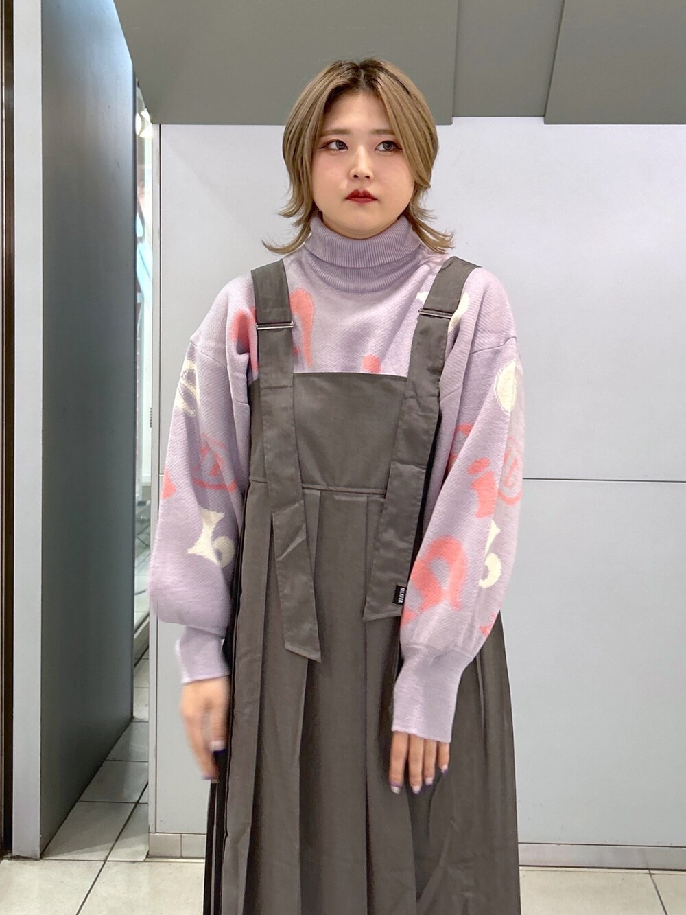 パープル系のニット/セーター、グレー系のジャンパースカート、ブラック系のショルダーバッグを着用したレディースの秋コーディネートの3枚目の写真