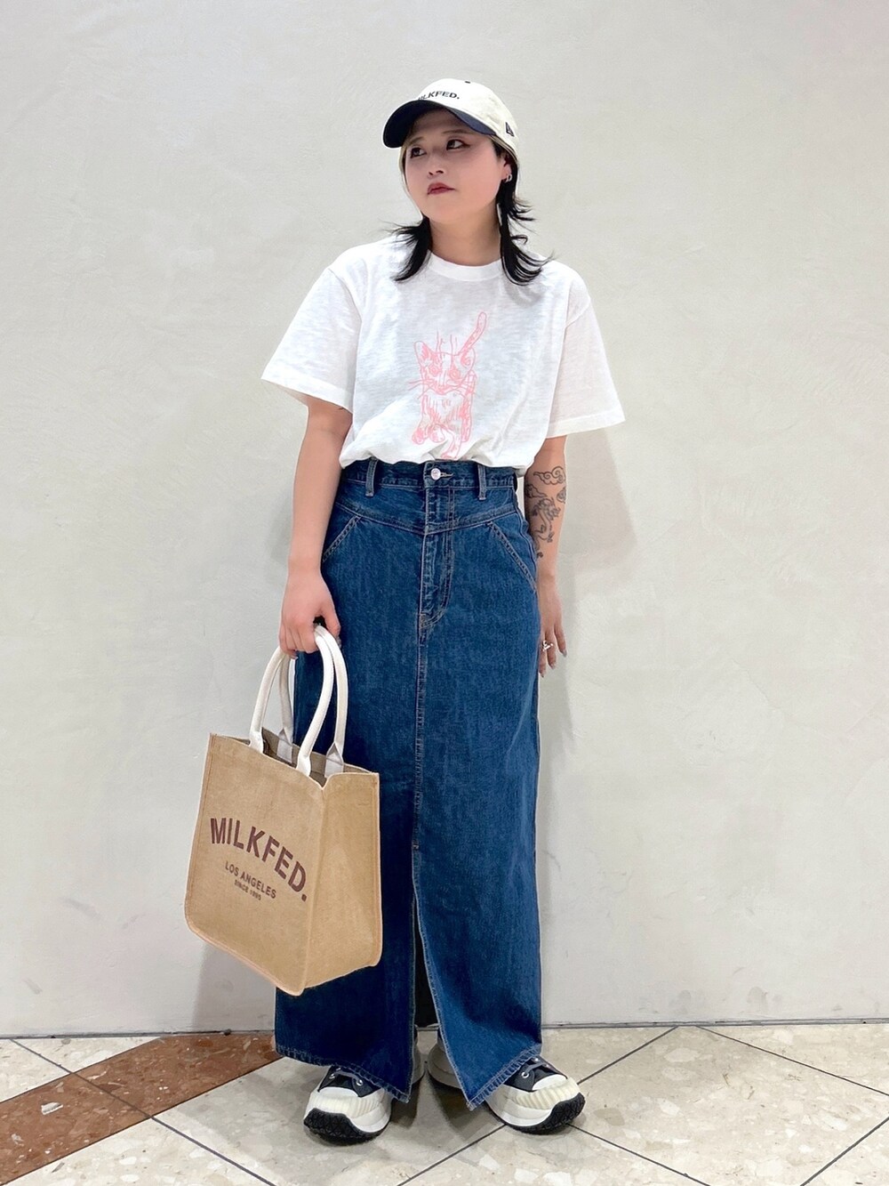 ホワイト系のTシャツ/カットソー、ブルー系のデニムスカート、ベージュ系のトートバッグを着用したレディースの春コーディネートの2枚目の写真