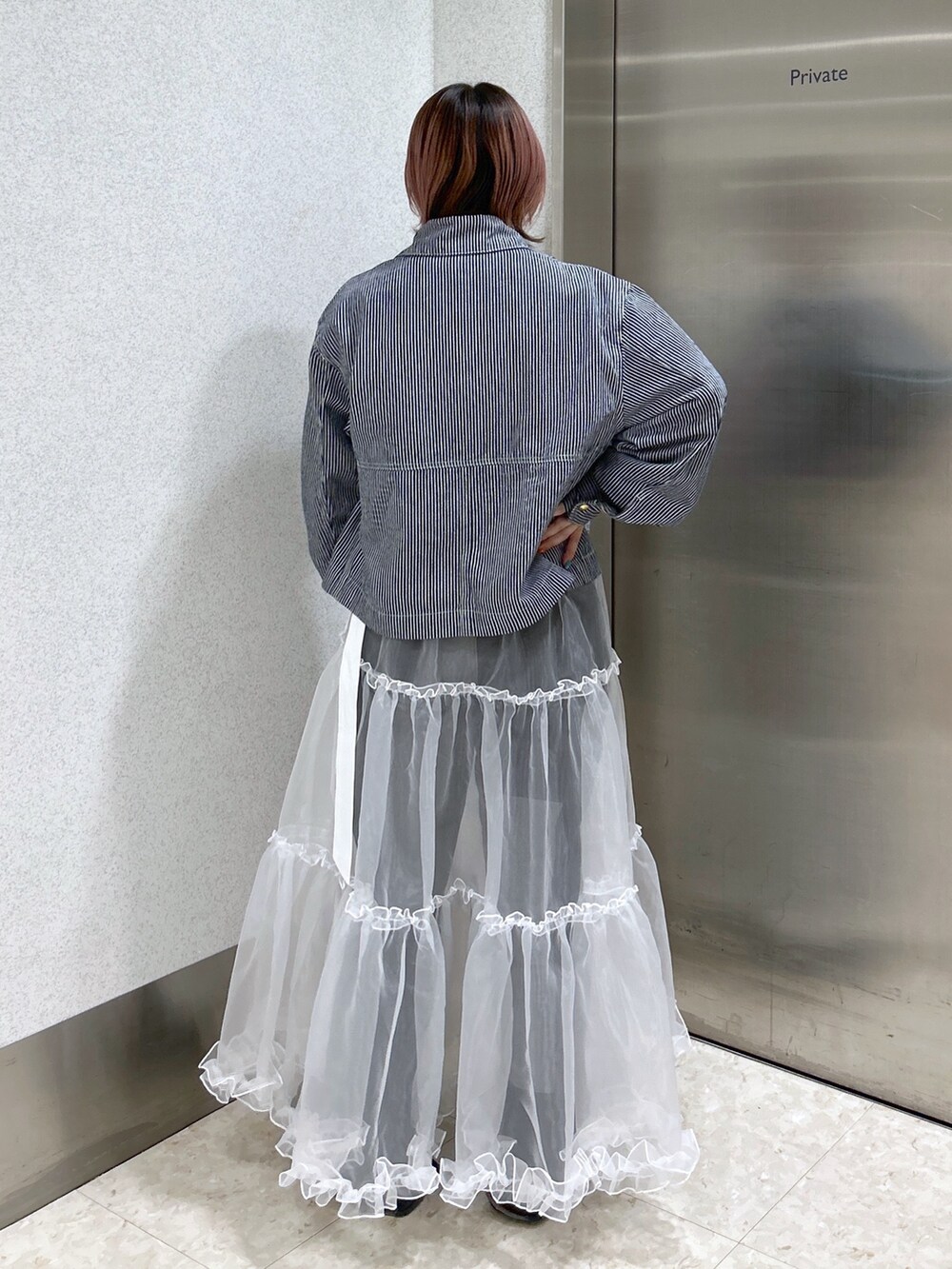 ホワイト系のスカート、ブラック系のデニムパンツ、ブラック系のブーツを着用したレディースの春コーディネートの4枚目の写真