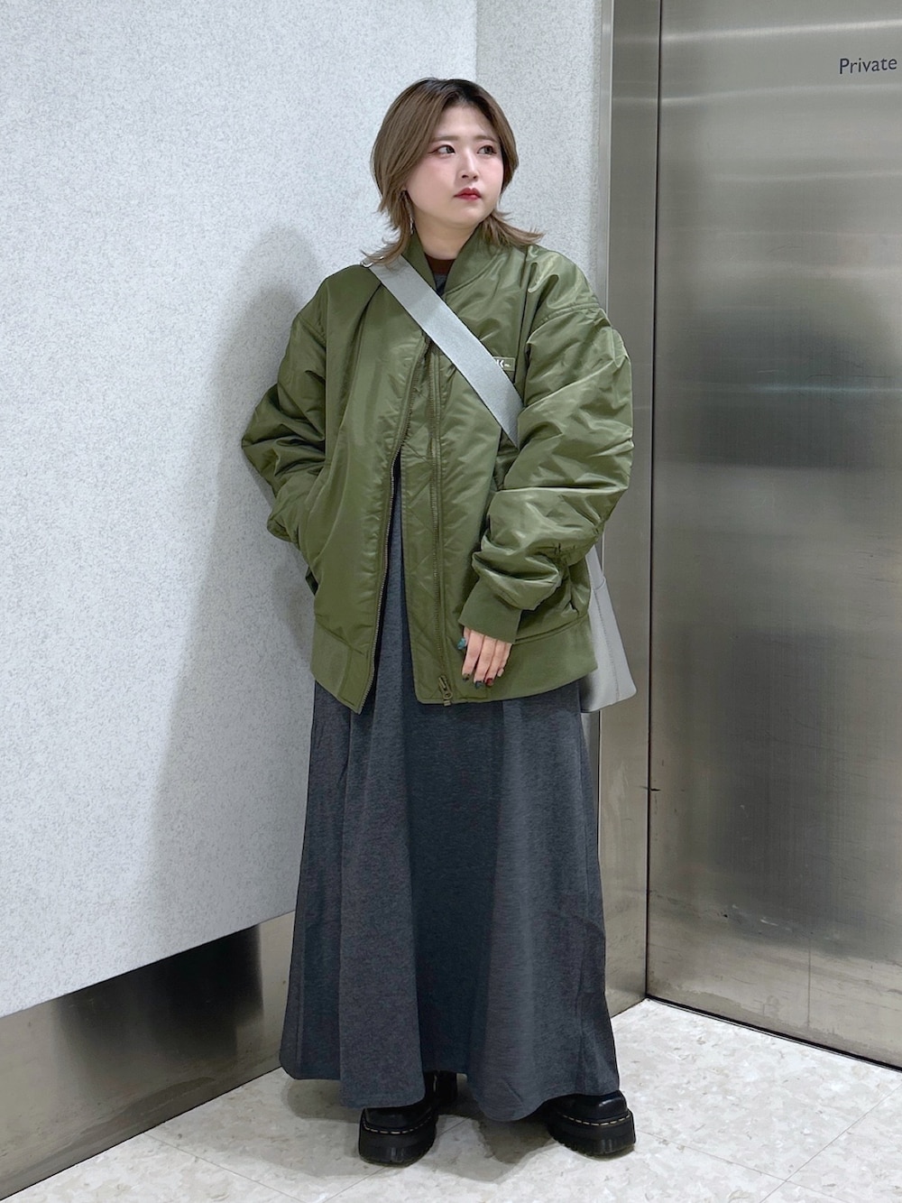 グレー系のワンピース、グリーン系のMA-1、シルバー系のショルダーバッグを着用したレディースの冬コーディネートの3枚目の写真