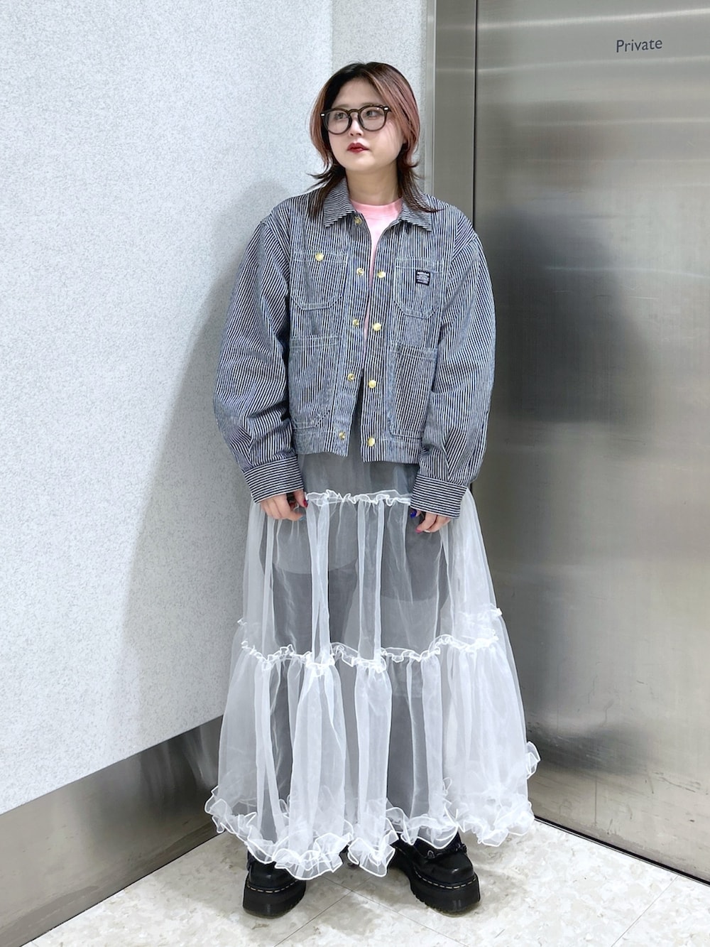 ホワイト系のスカート、ブラック系のデニムパンツ、ブラック系のブーツを着用したレディースの春コーディネートの2枚目の写真