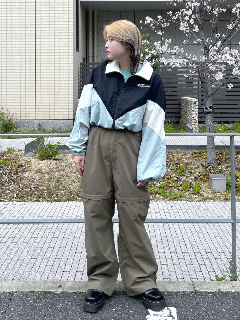 ブラック系のナイロンジャケット、グリーン系のTシャツ/カットソー、ブラック系のブーツを着用したレディースの春コーディネートの2枚目の写真