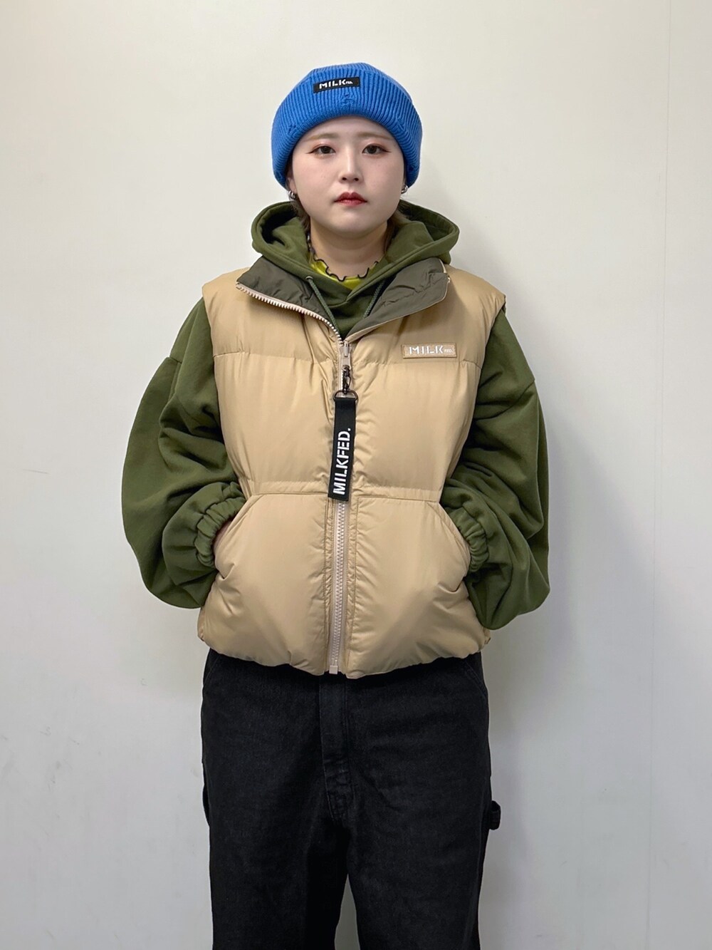 ベージュ系のダウンベスト、グリーン系のパーカー、ブラック系のサロペット/オーバーオールを着用したレディースの冬コーディネートの4枚目の写真