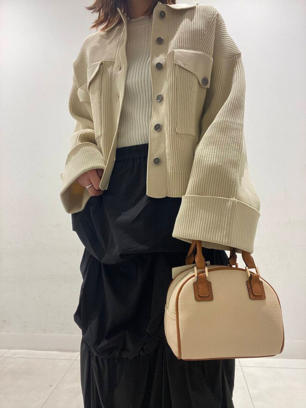 ブラック系のスカート、イエロー系のボストンバッグ、ベージュ系のニット/セーターを着用したレディースの冬コーディネートの3枚目の写真