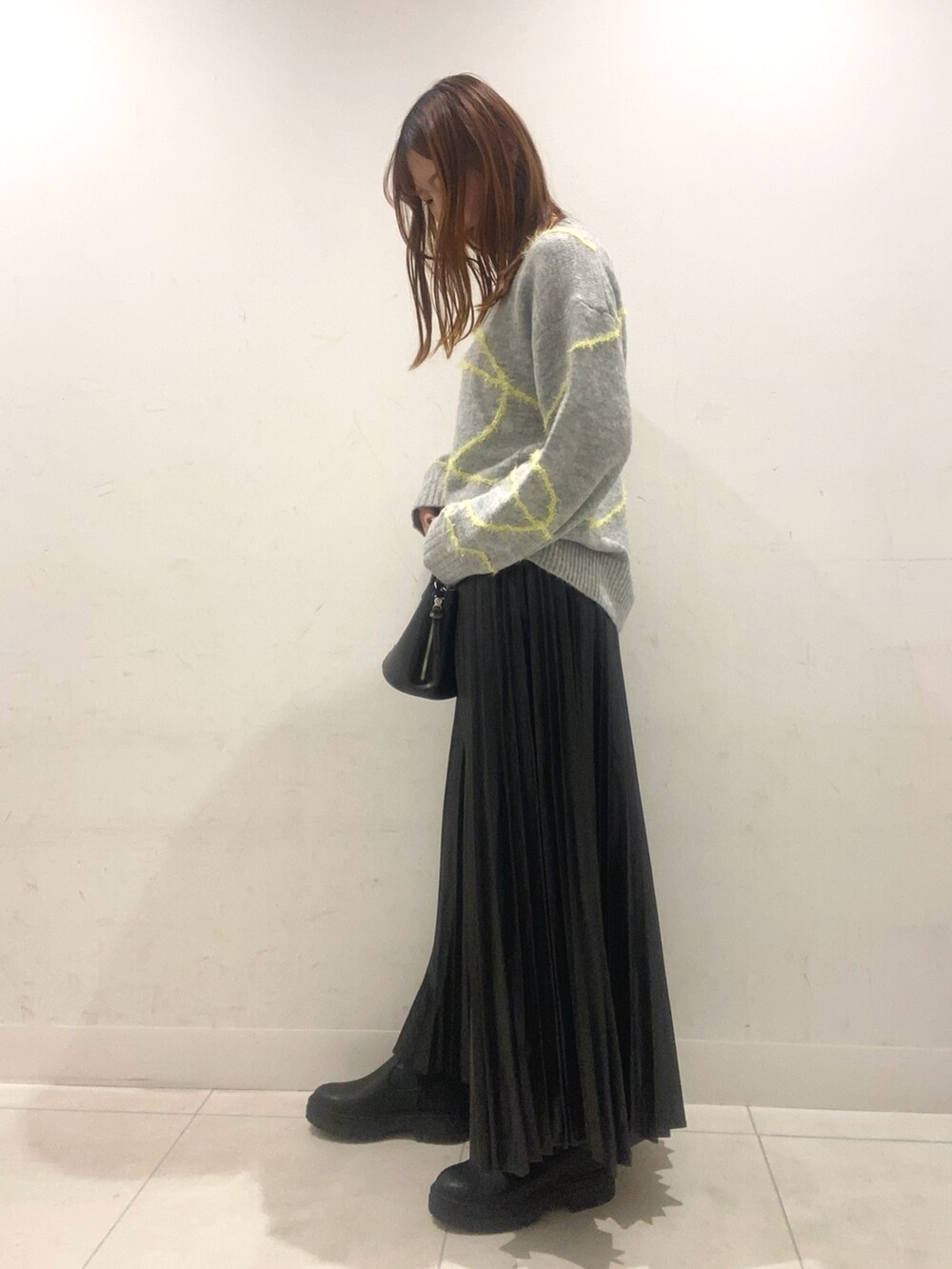 グレー系のニット/セーター、ブラック系のスカート、ブラック系のショルダーバッグを着用したレディースの秋コーディネートの2枚目の写真