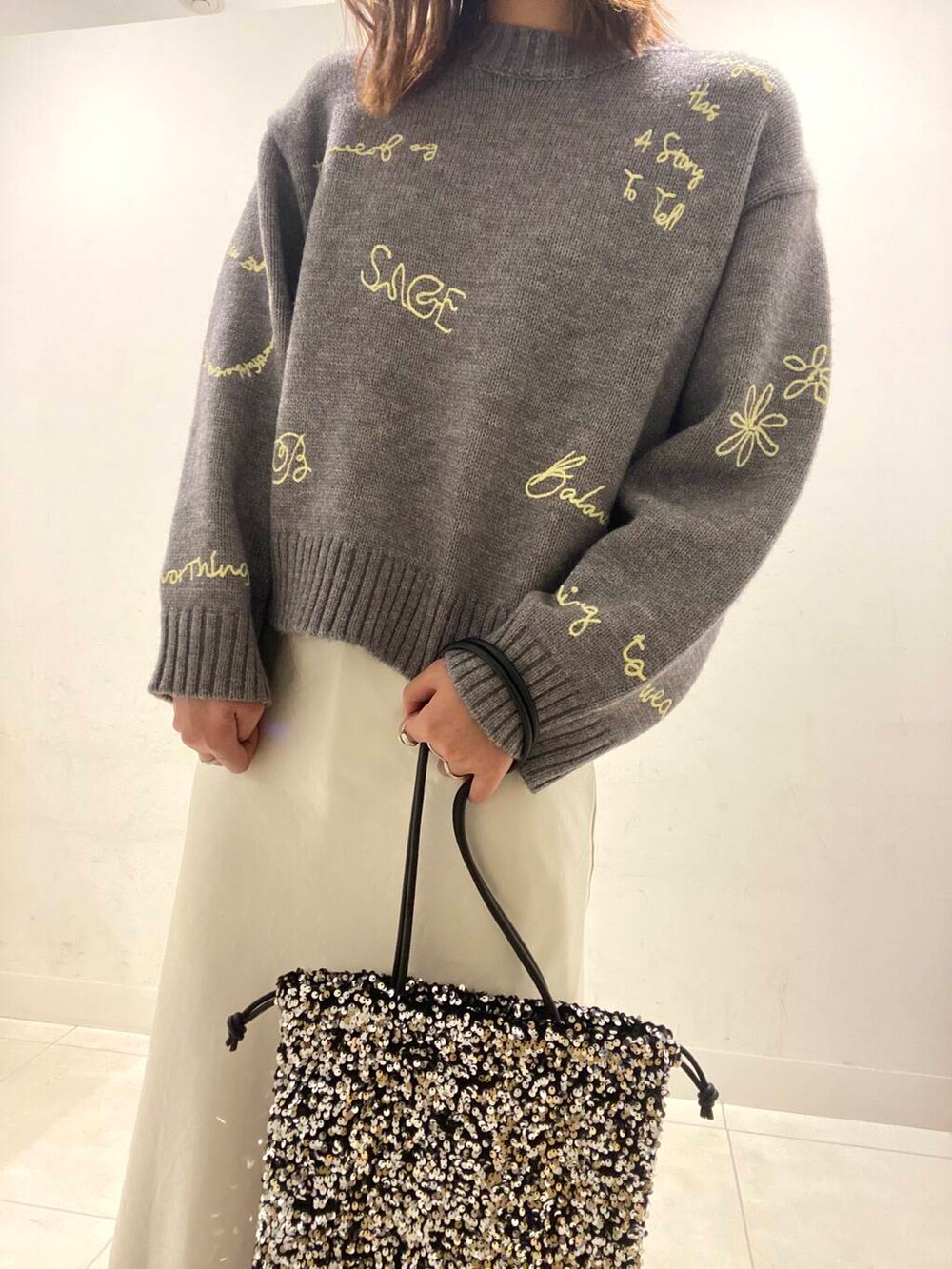 グレー系のニット/セーター、ホワイト系のスカート、シルバー系のトートバッグを着用したレディースの冬コーディネートの2枚目の写真