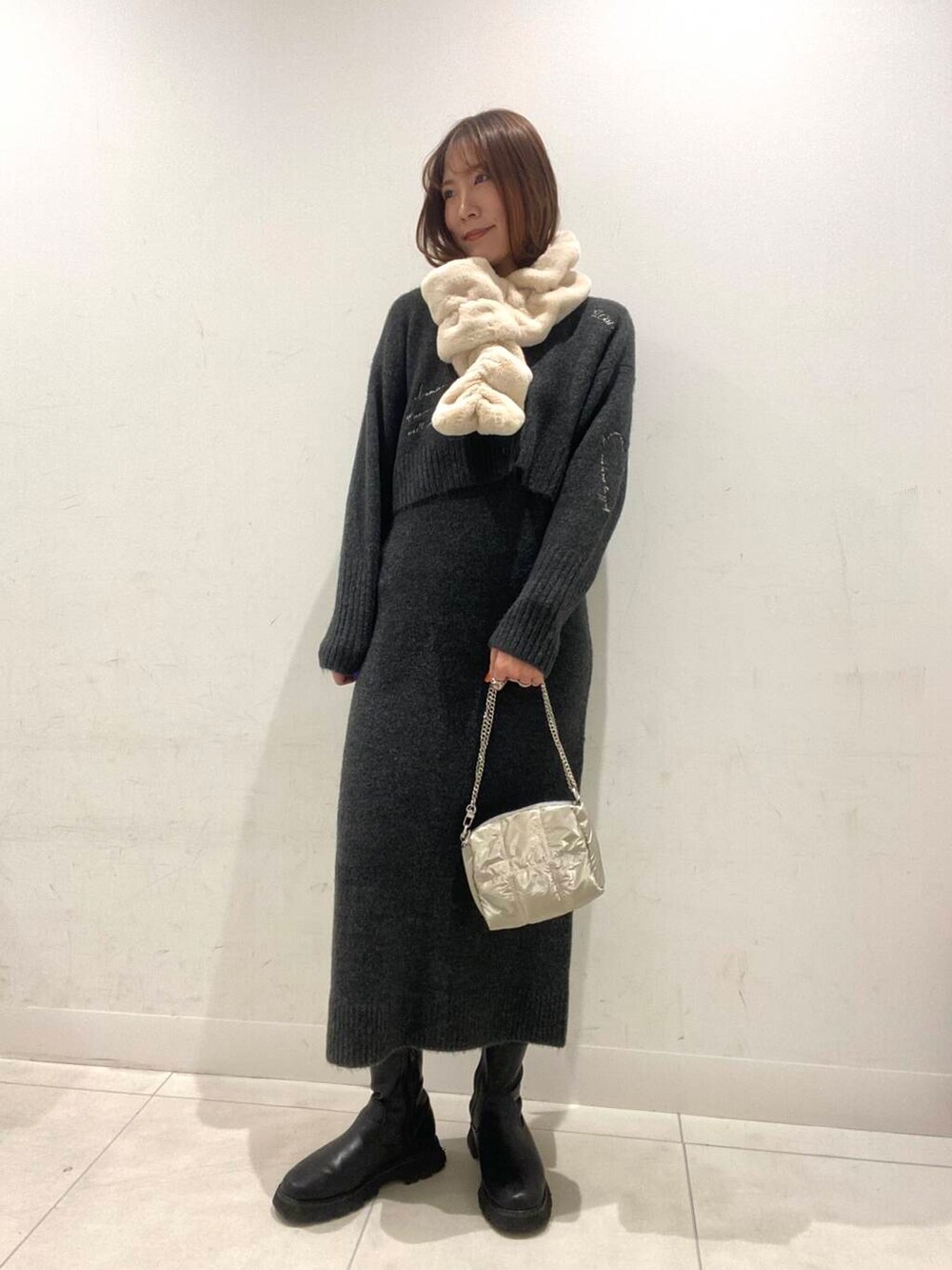 シルバー系のショルダーバッグ、グレー系のワンピース、ホワイト系のマフラーを着用したレディースの冬コーディネートの2枚目の写真