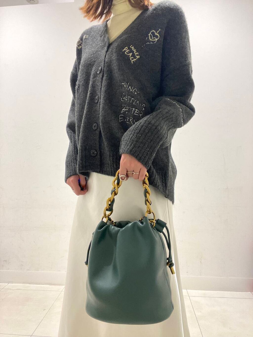 グリーン系のショルダーバッグ、ブラック系のブーツ、ホワイト系のスカートを着用したレディースの冬コーディネートの2枚目の写真