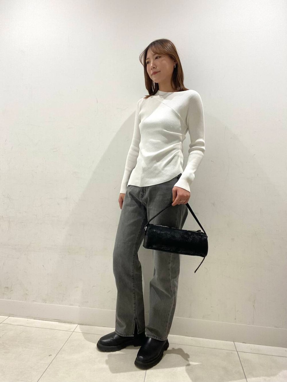 グレー系のデニムパンツ、ブラック系のハンドバッグ、ホワイト系のニット/セーターを着用したレディースの冬コーディネートの2枚目の写真