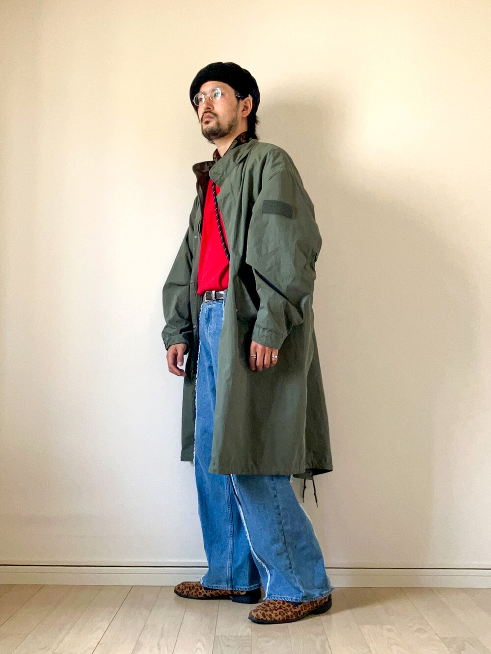 グリーン系のモッズコート、レッド系のTシャツ/カットソー、ブルー系のデニムパンツを着用したメンズの春コーディネートの2枚目の写真