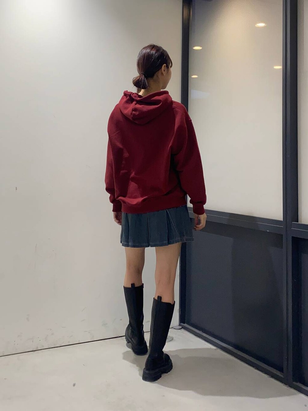 ブルー系のデニムスカート、ブラック系のブーツ、レッド系のパーカーを着用したレディースの秋コーディネートの2枚目の写真