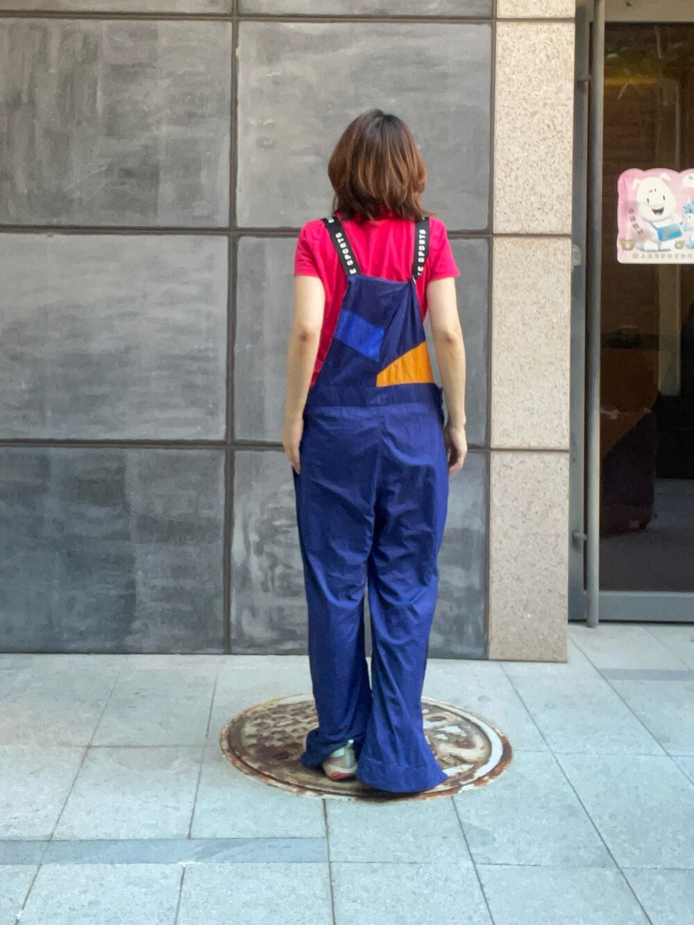 レッド系のポロシャツ、ブルー系のつなぎ/オールインワン、ベージュ系のレインシューズを着用したレディースの秋コーディネートの5枚目の写真