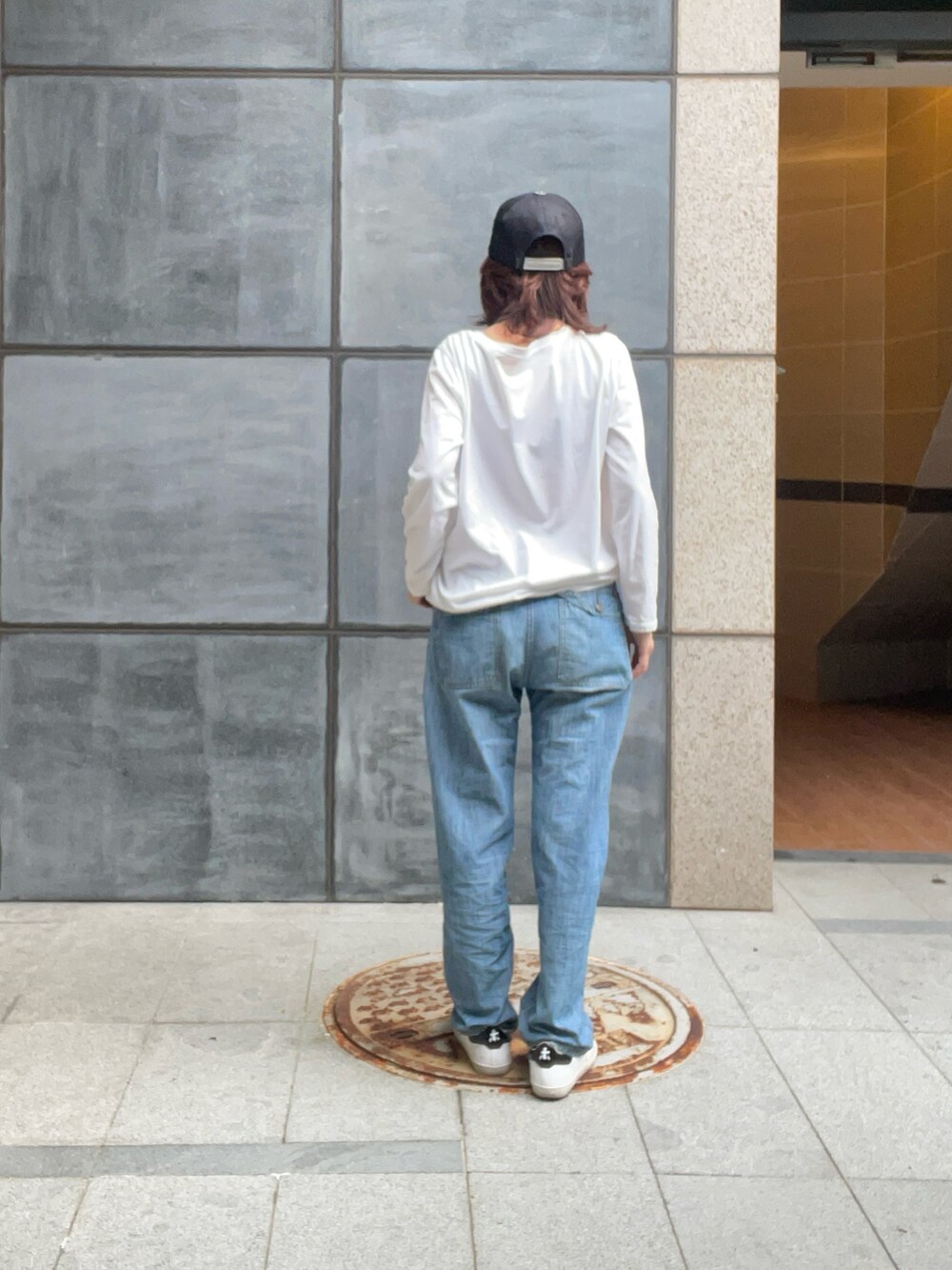 ブルー系のデニムパンツ、ホワイト系のスニーカー、ブルー系のキャップを着用したレディースの春コーディネートの2枚目の写真