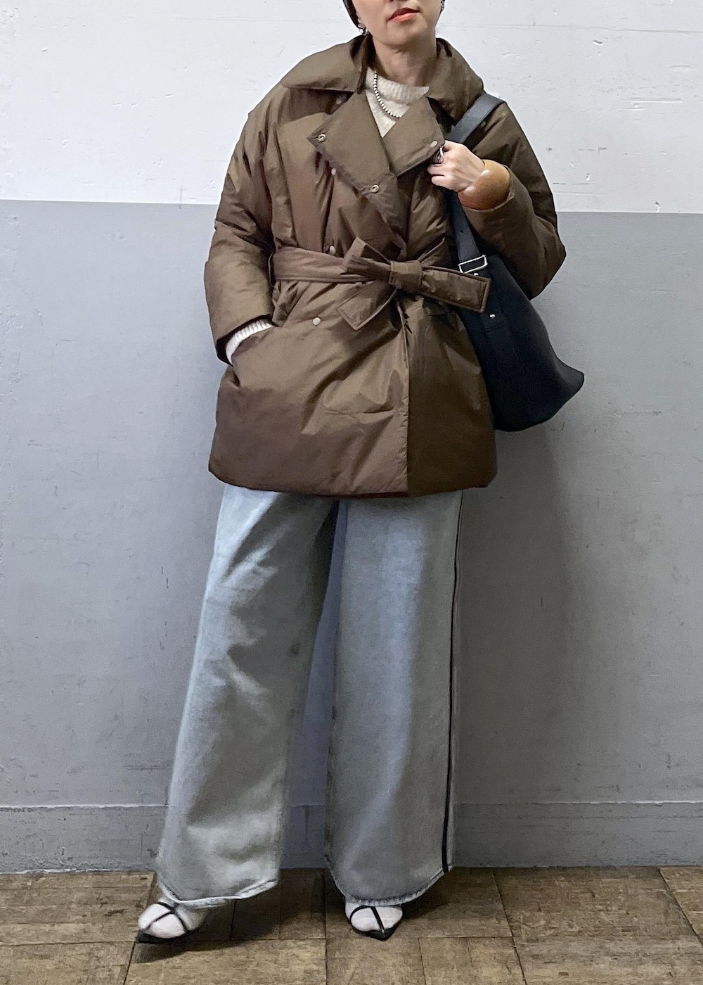 ブルー系のデニムパンツ、ブラック系のショルダーバッグ、ベージュ系のニット/セーターを着用したレディースの冬コーディネートの2枚目の写真