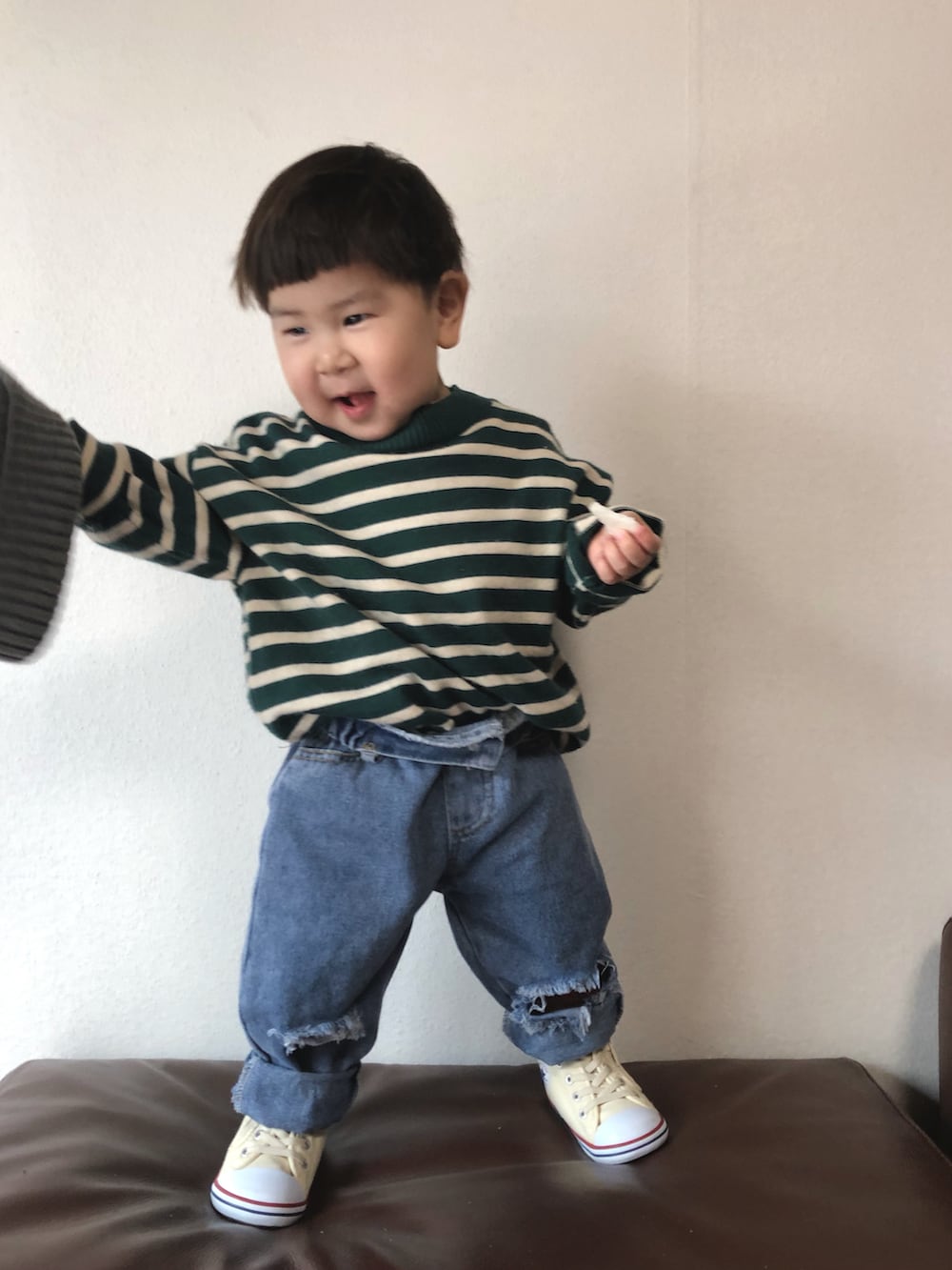 グリーン系のスウェット、ブルー系のデニムパンツ、ホワイト系のスニーカーを着用したキッズの冬コーディネートの3枚目の写真