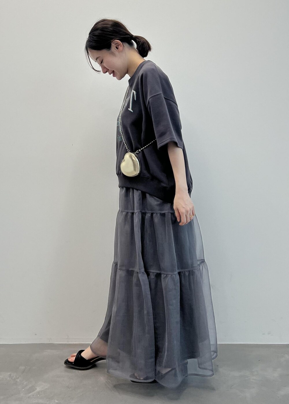 ゴールド系のショルダーバッグ、グレー系のスカート、ブラック系のサンダルを着用したレディースの春コーディネートの2枚目の写真