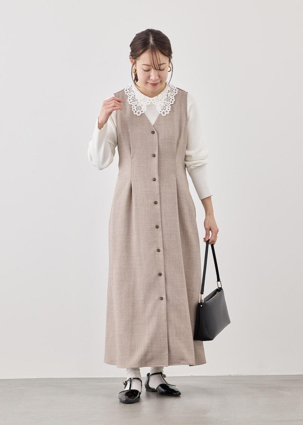 ブラック系のショルダーバッグ、ホワイト系のニット/セーター、ベージュ系のジャンパースカートを着用したレディースの春コーディネートの2枚目の写真