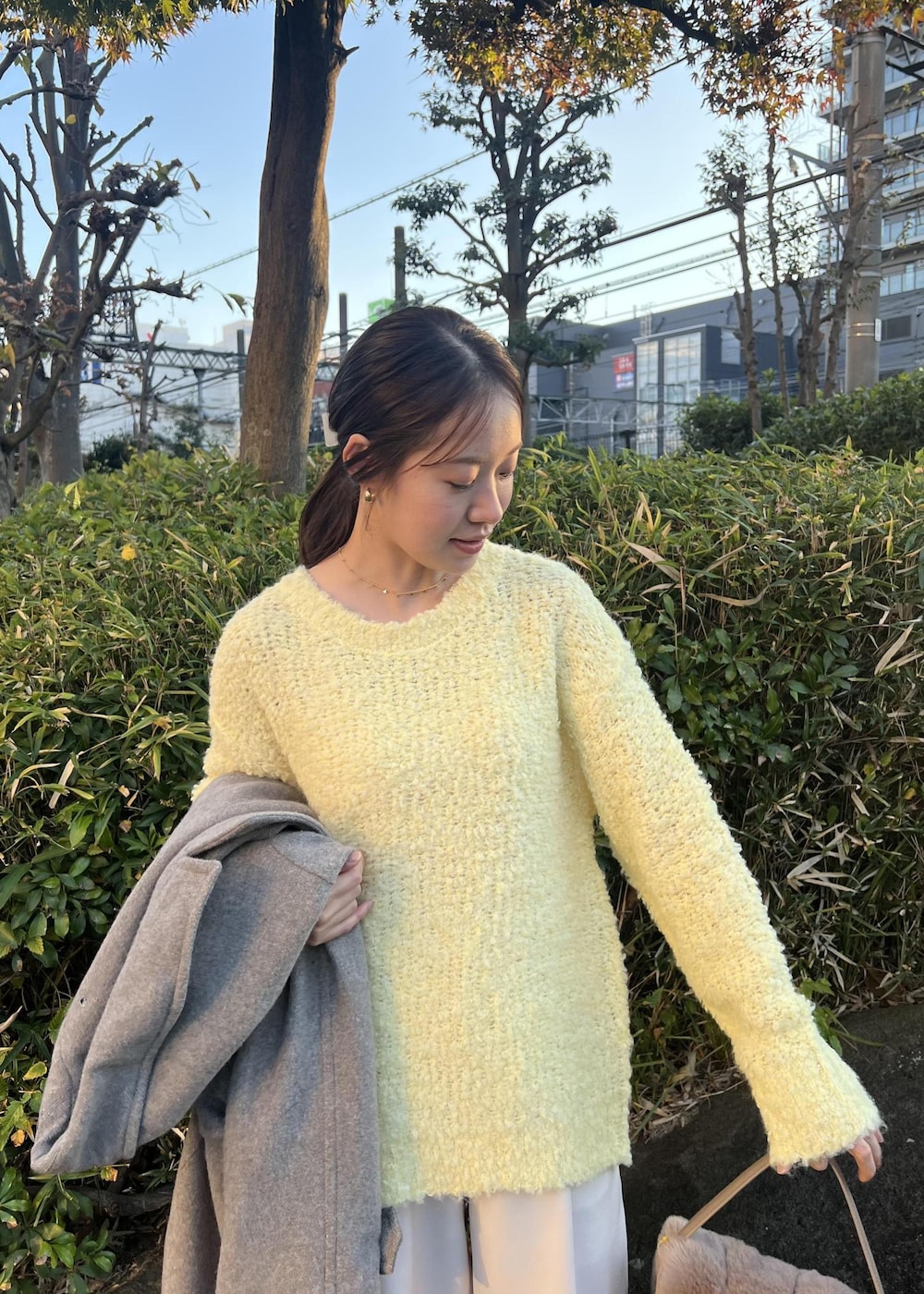 ベージュ系のチェスターコート、ブラウン系のショルダーバッグ、イエロー系のニット/セーターを着用したレディースの秋コーディネートの8枚目の写真