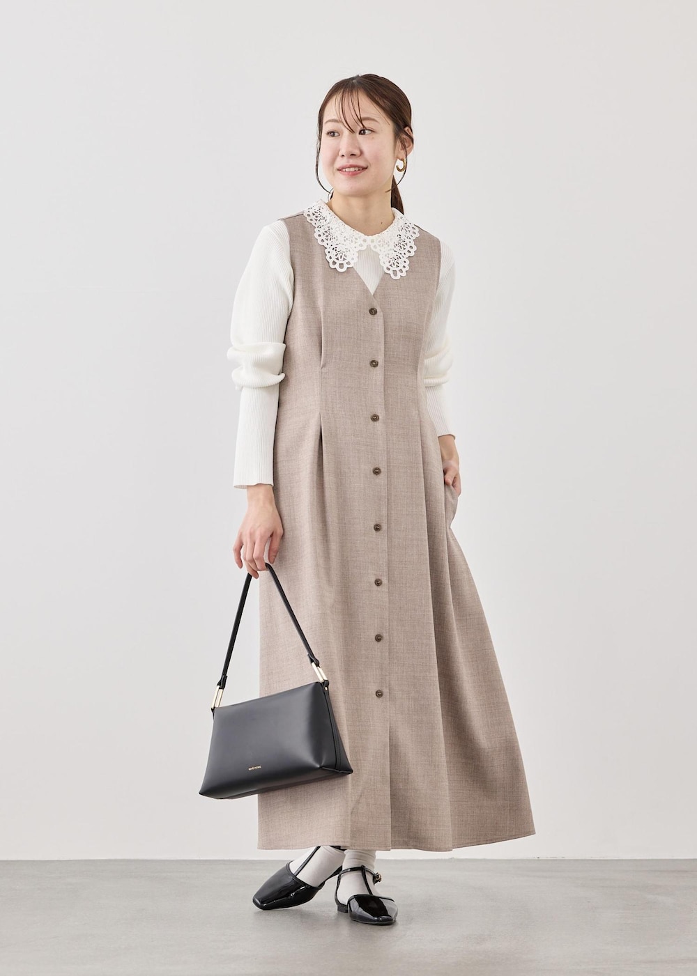 ブラック系のショルダーバッグ、ホワイト系のニット/セーター、ベージュ系のジャンパースカートを着用したレディースの春コーディネートの3枚目の写真