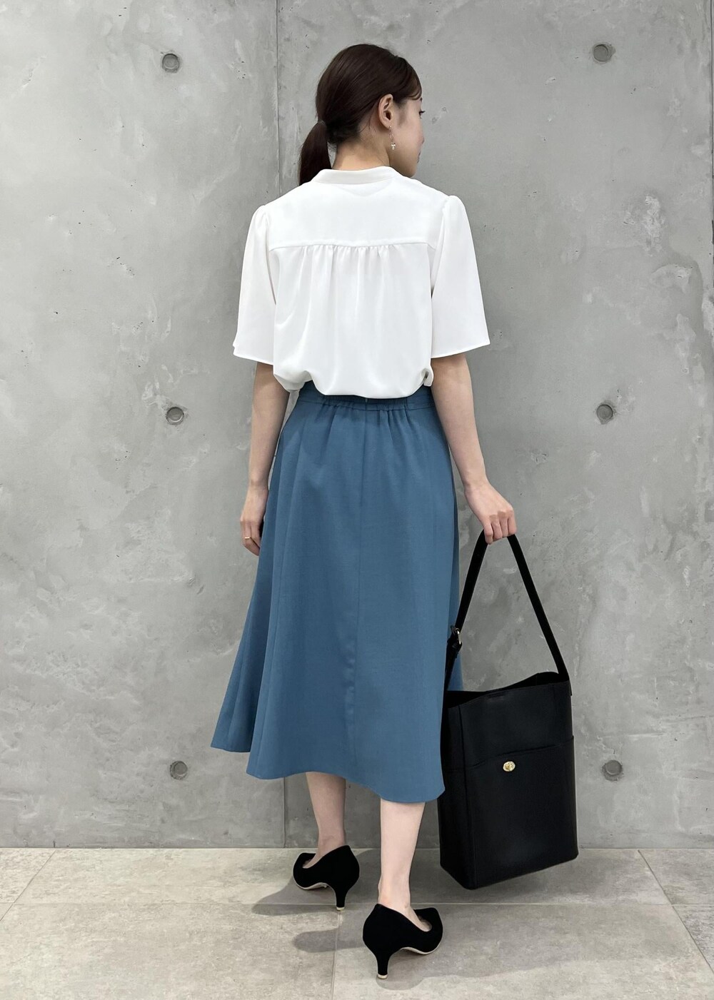 ブラック系のパンプス、ブルー系のスカート、ブラック系のショルダーバッグを着用したレディースの春コーディネートの3枚目の写真