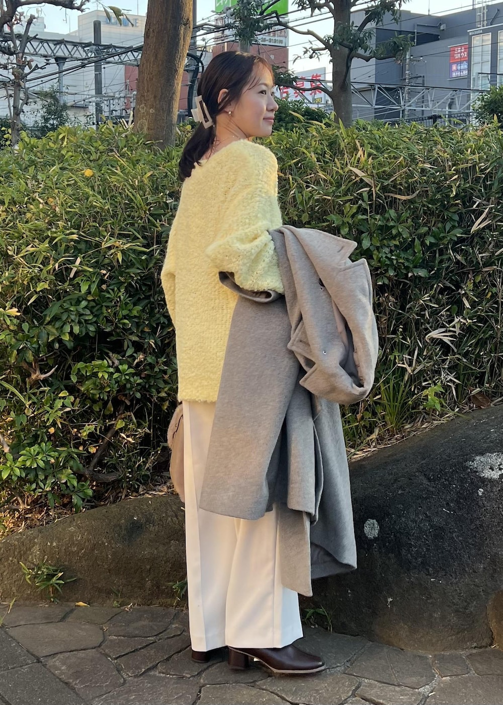 ベージュ系のチェスターコート、ブラウン系のショルダーバッグ、イエロー系のニット/セーターを着用したレディースの秋コーディネートの7枚目の写真