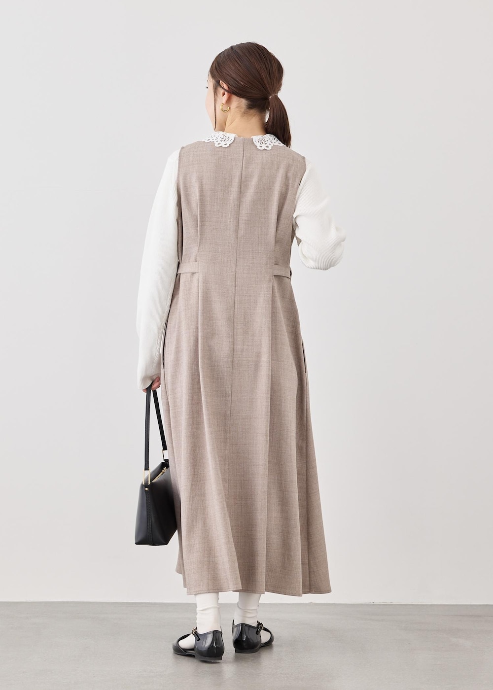 ブラック系のショルダーバッグ、ホワイト系のニット/セーター、ベージュ系のジャンパースカートを着用したレディースの春コーディネートの6枚目の写真