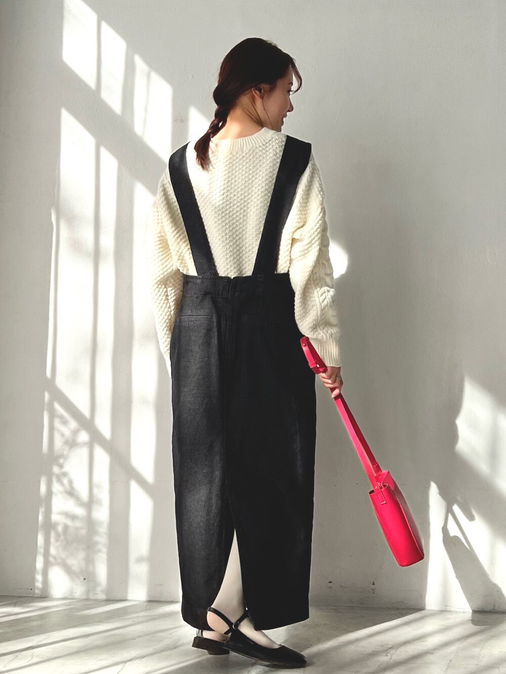 ブラック系のジャンパースカート、ホワイト系のニット/セーター、ピンク系のショルダーバッグを着用したレディースの冬コーディネートの3枚目の写真