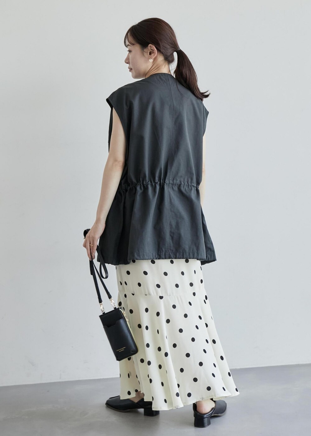 グレー系のベスト、ホワイト系のスカート、ブラック系のパンプスを着用したレディースの夏コーディネートの3枚目の写真