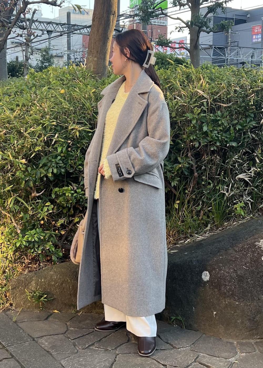 ベージュ系のチェスターコート、ブラウン系のショルダーバッグ、イエロー系のニット/セーターを着用したレディースの秋コーディネートの2枚目の写真