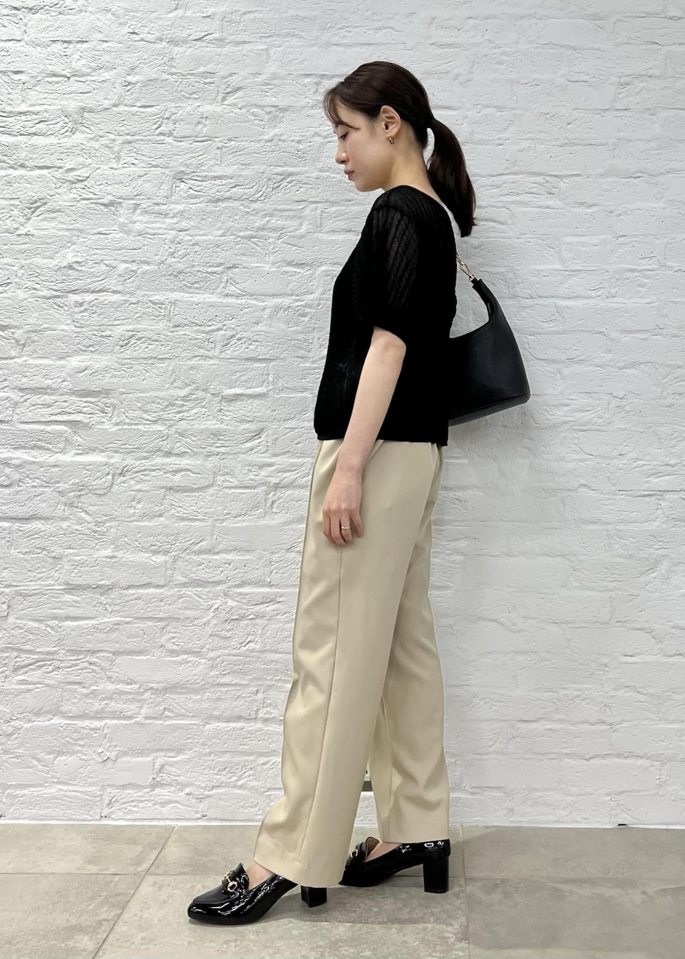 ブラック系のローファー、ブラック系のショルダーバッグ、ベージュ系のスラックスを着用したレディースの夏コーディネートの2枚目の写真