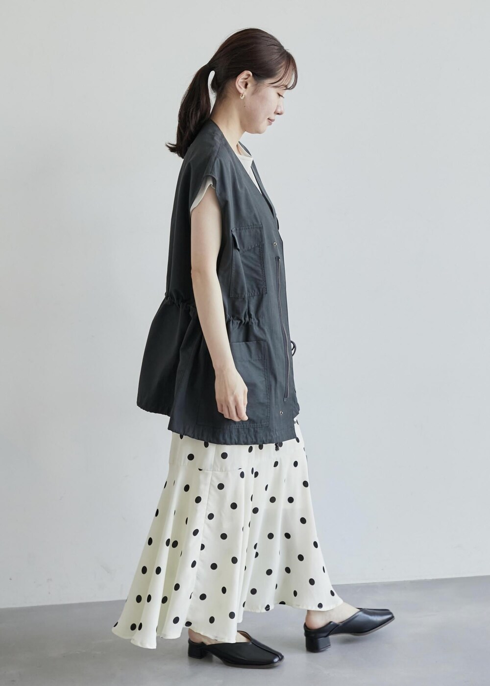 グレー系のベスト、ホワイト系のスカート、ブラック系のパンプスを着用したレディースの夏コーディネートの2枚目の写真